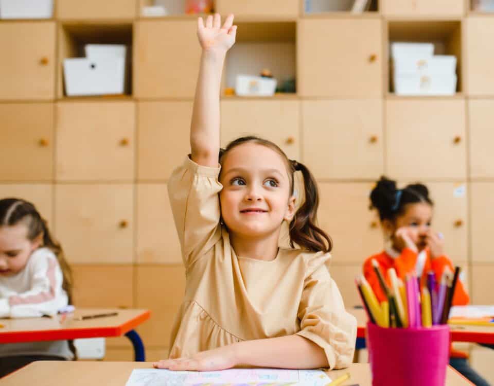 A girl in a classroom raising her hand