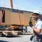 Construction worker supervising loading of prefabricated house module onto truck