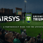 Co-branded graphic announcing the partnership between Airsys and Greenville Triumph. On a dark background, the white Airsys logo is placed on the left, and the green-and-yellow Greenville Triumph crest logo is on the right. Below the logos, green text reads: "A PARTNERSHIP MADE FOR THE UPSTATE" over a faint background photo of soccer stadium lights.